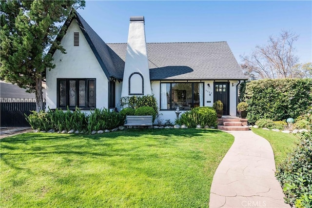 rear view of property with a chimney, roof with shingles, fence, a yard, and stucco siding