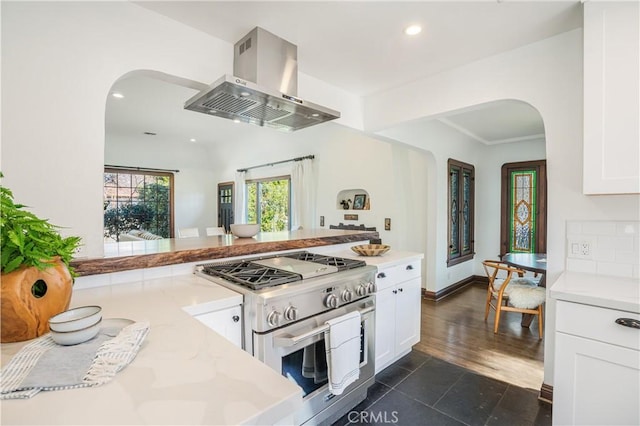 kitchen featuring arched walkways, light stone counters, island range hood, white cabinets, and high end range