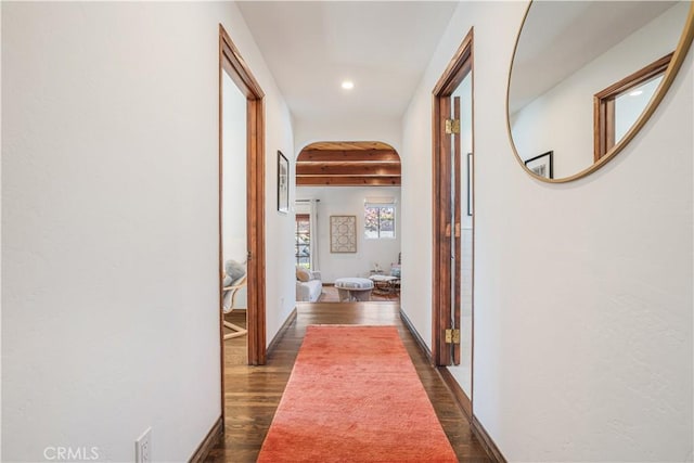 hall with arched walkways, dark wood-style flooring, recessed lighting, beamed ceiling, and baseboards