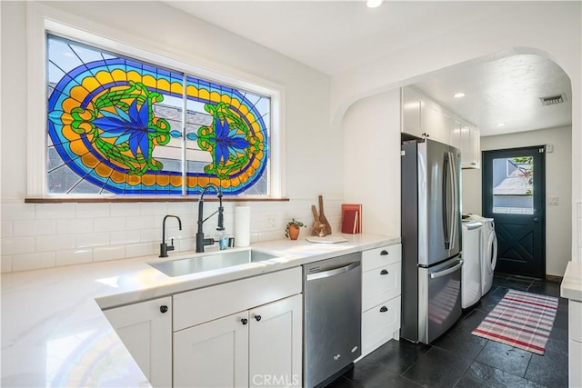 kitchen with washing machine and clothes dryer, stainless steel appliances, light countertops, white cabinetry, and a sink