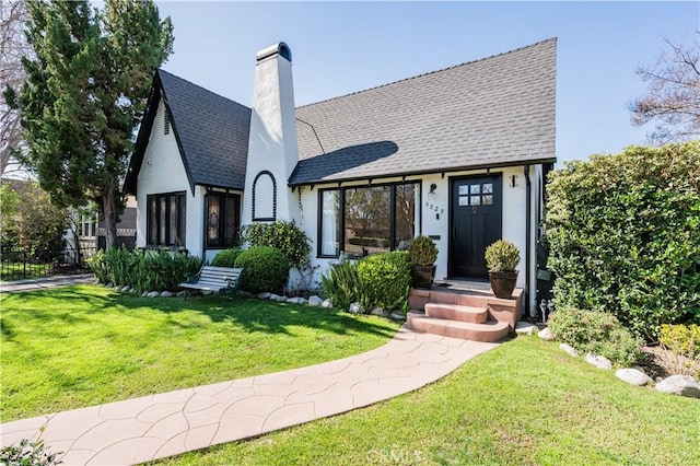 view of front of property with a shingled roof, a chimney, a front lawn, and stucco siding