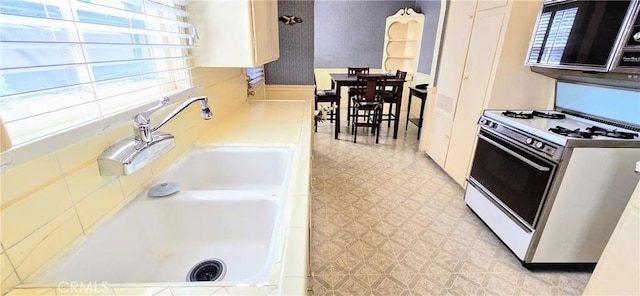 kitchen featuring light floors, light countertops, white range with gas cooktop, a sink, and wallpapered walls