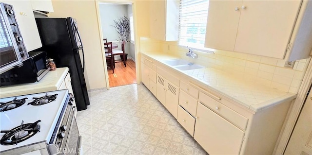 kitchen featuring white range with gas cooktop, a sink, light countertops, light floors, and backsplash