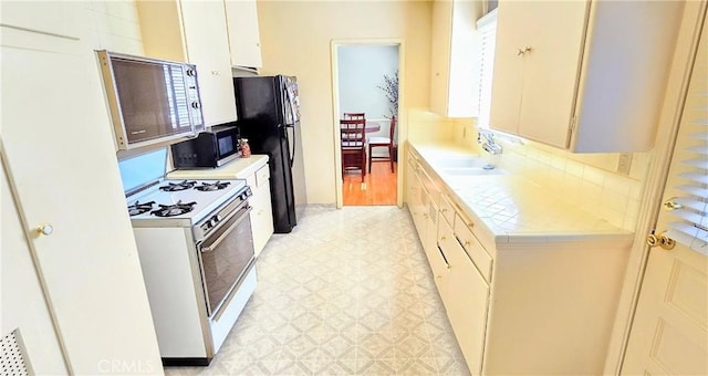 kitchen featuring tile counters, freestanding refrigerator, white gas stove, light floors, and a sink