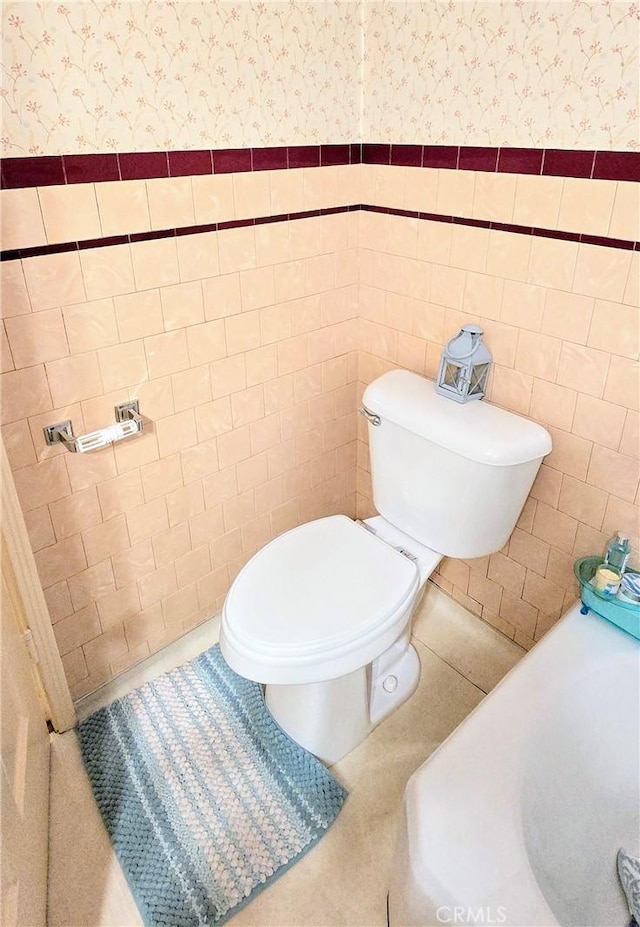 bathroom featuring a wainscoted wall, tile patterned flooring, toilet, and wallpapered walls