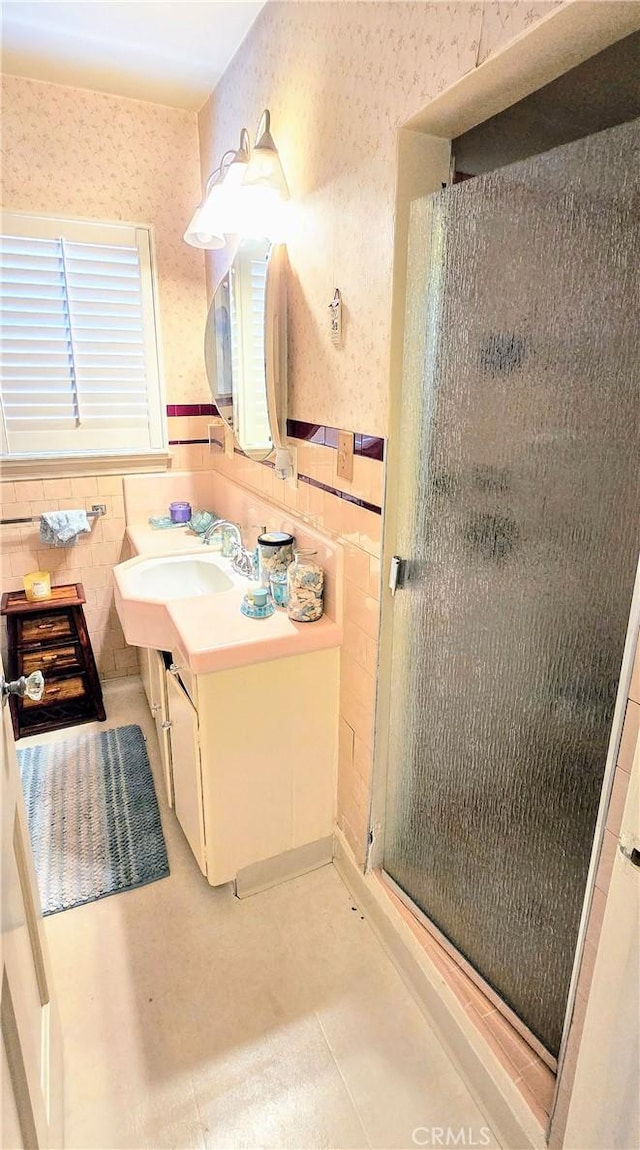 full bath with tile walls, a stall shower, wainscoting, vanity, and wallpapered walls