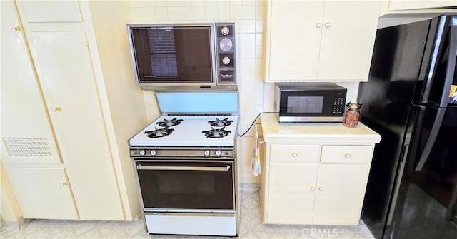 kitchen with freestanding refrigerator, white cabinets, light countertops, and white gas stove