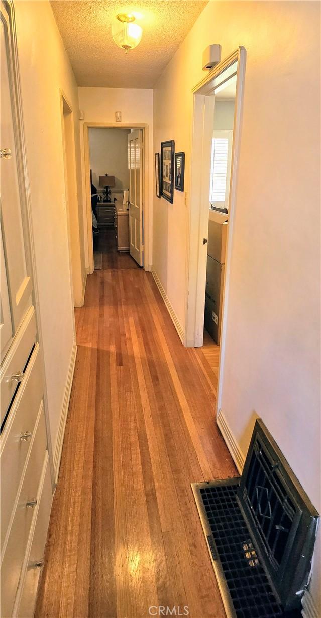 hallway featuring a textured ceiling, wood-type flooring, and baseboards