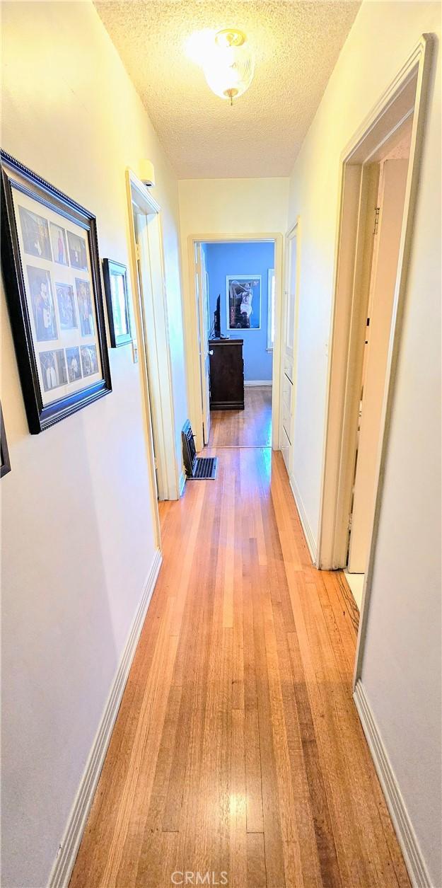 hall featuring a textured ceiling, light wood-style flooring, and baseboards