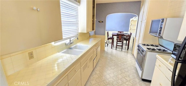 kitchen with arched walkways, white gas stove, a sink, white cabinetry, and light floors