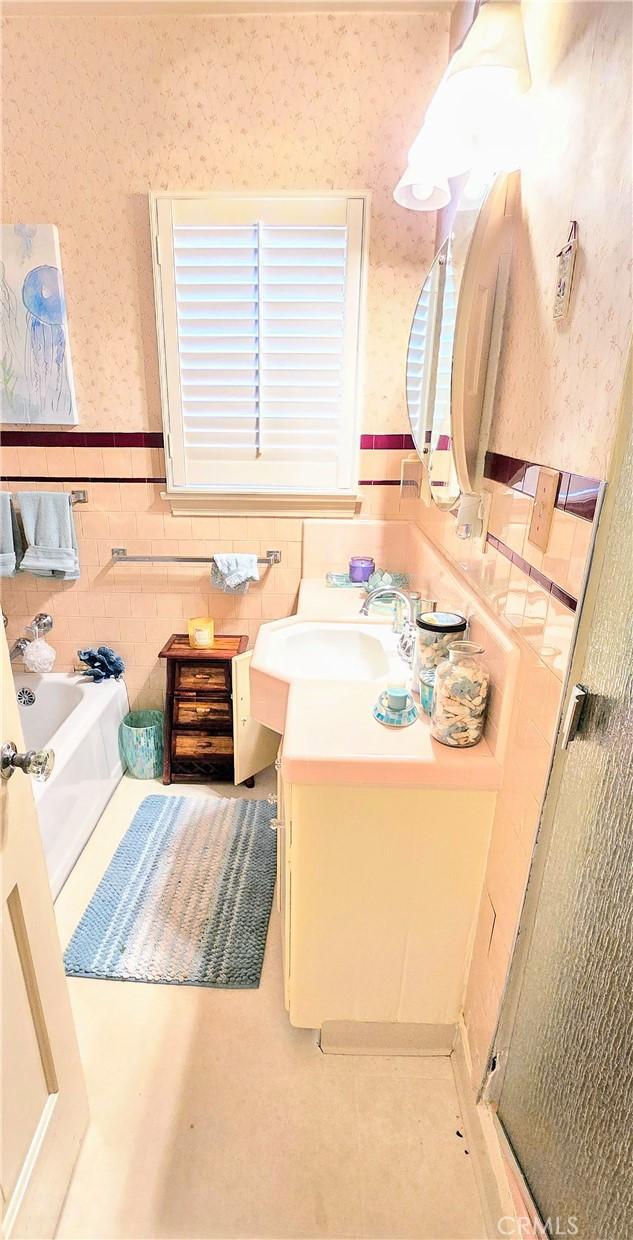 full bathroom featuring wallpapered walls, wainscoting, a bath, vanity, and tile walls