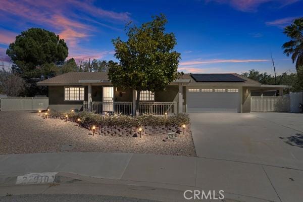 single story home with concrete driveway, fence, an attached garage, and solar panels