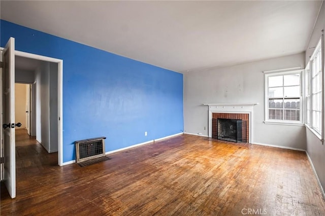 unfurnished living room with heating unit, a brick fireplace, baseboards, and hardwood / wood-style floors