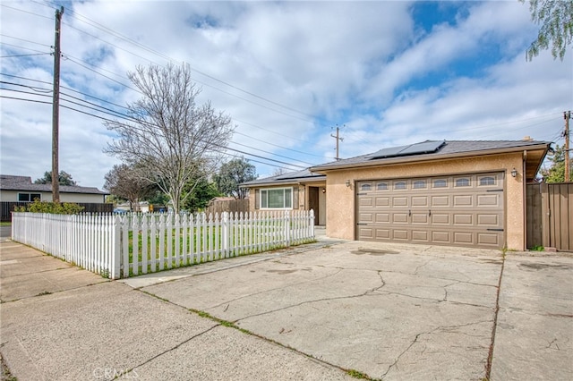 ranch-style house with a fenced front yard, concrete driveway, a garage, and solar panels