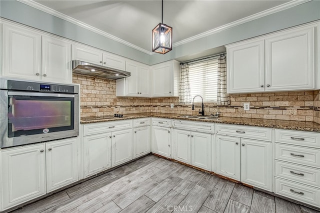 kitchen with pendant lighting, white cabinets, a sink, oven, and under cabinet range hood