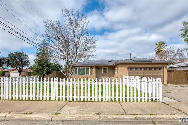 ranch-style house with a garage, a fenced front yard, roof mounted solar panels, and concrete driveway