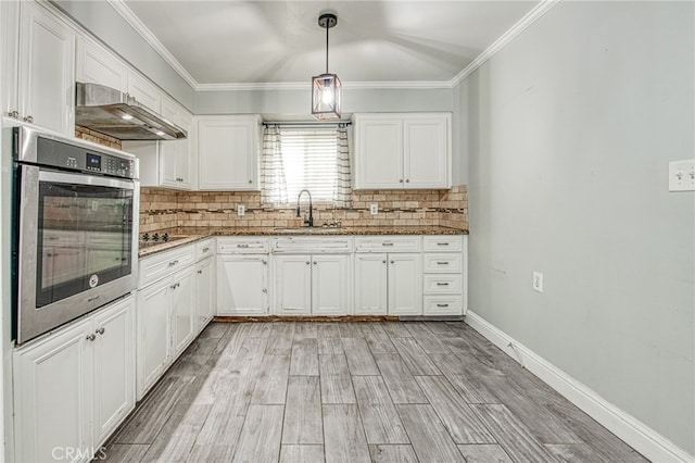 kitchen featuring under cabinet range hood, a sink, stainless steel oven, white cabinetry, and decorative backsplash