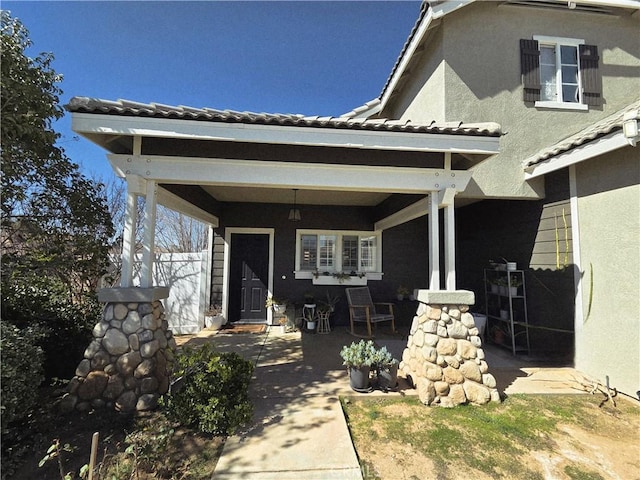 entrance to property with a tile roof, a patio area, fence, and stucco siding