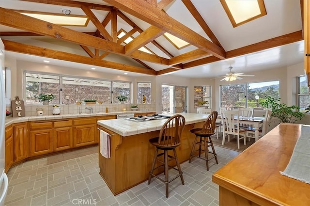 kitchen with tile countertops, white stovetop, a kitchen island, tasteful backsplash, and a kitchen bar