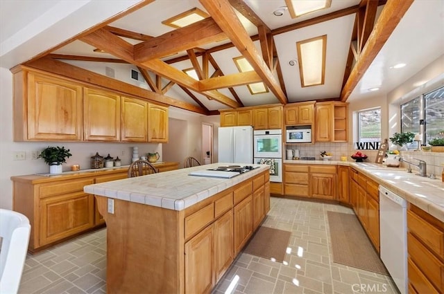 kitchen with white appliances, tile countertops, a kitchen island, backsplash, and a sink