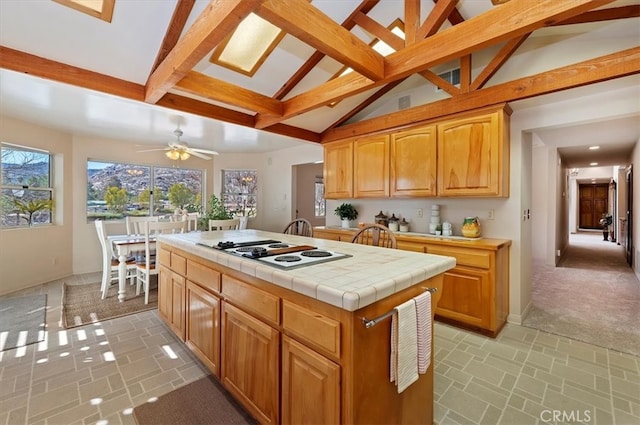 kitchen featuring white electric stovetop, a ceiling fan, tile countertops, lofted ceiling with beams, and a kitchen island