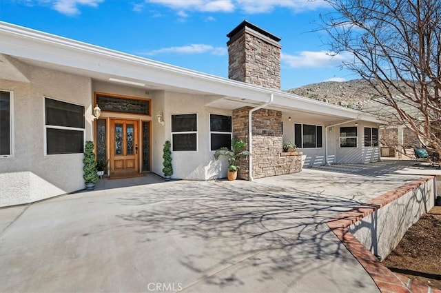 doorway to property featuring stone siding, a chimney, and stucco siding