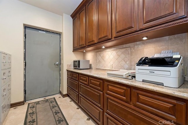 kitchen featuring light tile patterned floors, baseboards, backsplash, and light stone countertops