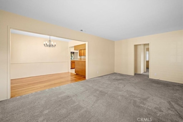 unfurnished living room with carpet, visible vents, and an inviting chandelier