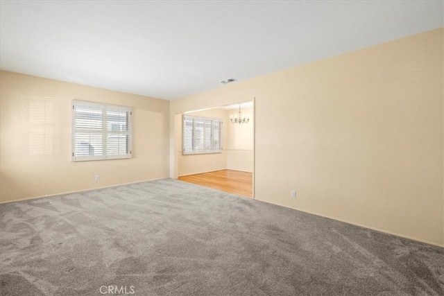 unfurnished room featuring a chandelier, visible vents, and light carpet