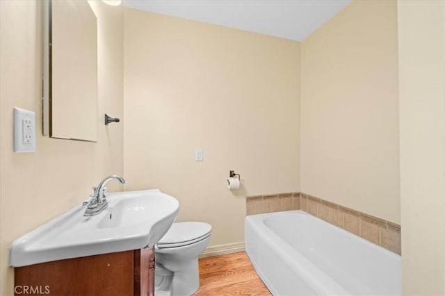 bathroom featuring baseboards, toilet, wood finished floors, vanity, and a bath