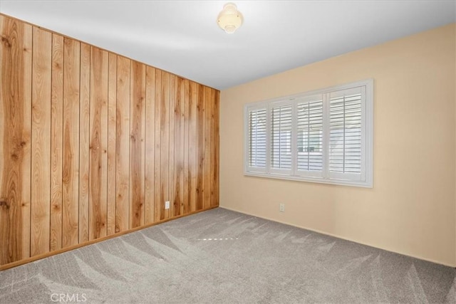 carpeted empty room featuring wood walls