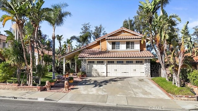 mediterranean / spanish house with an attached garage, a tiled roof, stone siding, and driveway