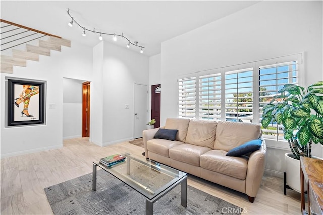 living area featuring track lighting, wood finished floors, a towering ceiling, and baseboards