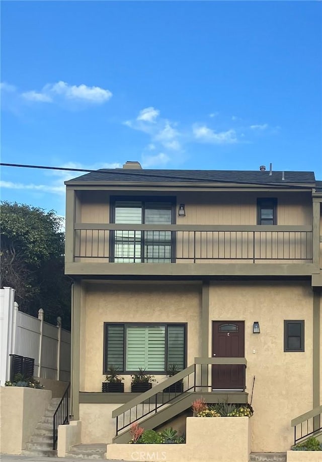 view of front facade featuring fence, a balcony, and stucco siding