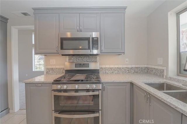 kitchen with light tile patterned floors, light stone counters, visible vents, gray cabinetry, and appliances with stainless steel finishes