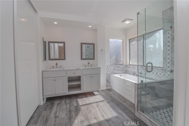 bathroom with double vanity, wood finished floors, a garden tub, and a stall shower