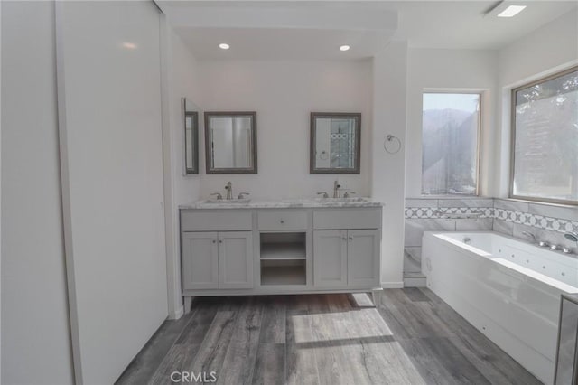 bathroom with double vanity, a jetted tub, wood finished floors, and a sink