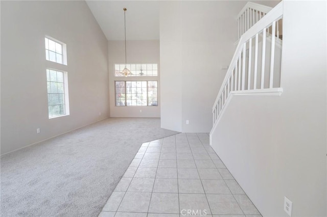 spare room featuring stairs, light tile patterned floors, light colored carpet, and a towering ceiling