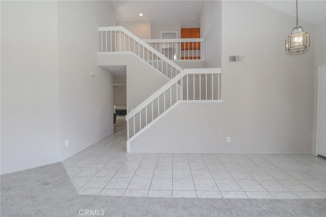 stairway featuring tile patterned flooring, carpet flooring, visible vents, and a towering ceiling