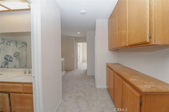 corridor featuring light colored carpet, baseboards, and a sink