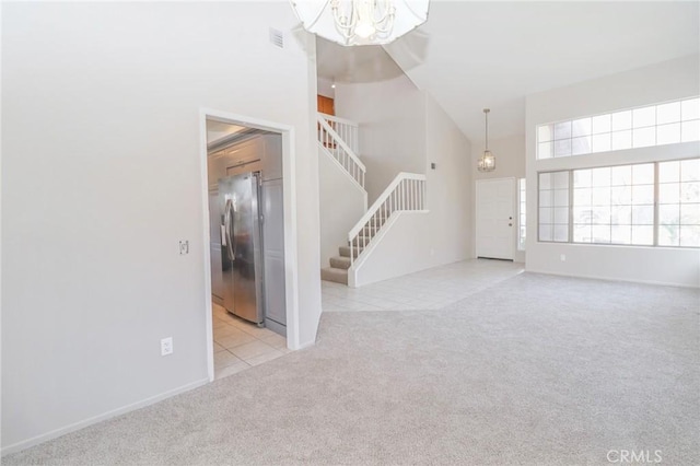 unfurnished living room with tile patterned flooring, a chandelier, stairway, carpet floors, and a high ceiling