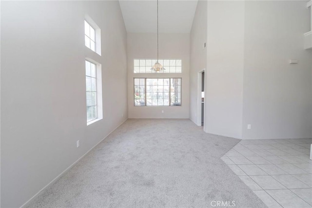 empty room featuring light tile patterned floors, light colored carpet, a towering ceiling, and a chandelier