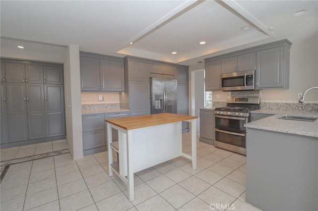 kitchen featuring butcher block countertops, gray cabinetry, a sink, appliances with stainless steel finishes, and a raised ceiling