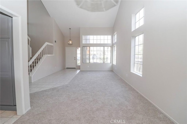 unfurnished living room with baseboards, carpet floors, tile patterned flooring, stairs, and a towering ceiling