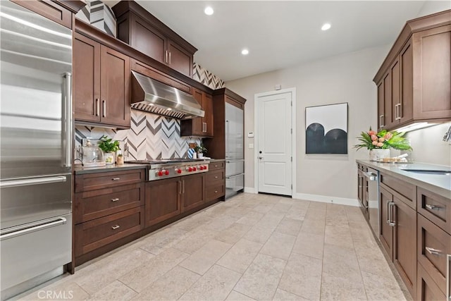 kitchen with recessed lighting, stainless steel appliances, a sink, wall chimney range hood, and tasteful backsplash