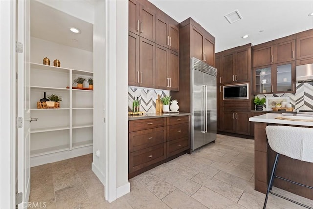 kitchen with built in appliances, light countertops, glass insert cabinets, and decorative backsplash