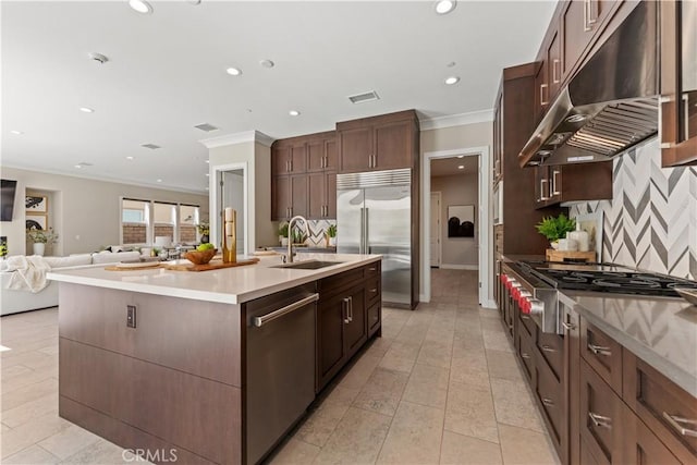 kitchen with light countertops, appliances with stainless steel finishes, a sink, an island with sink, and under cabinet range hood