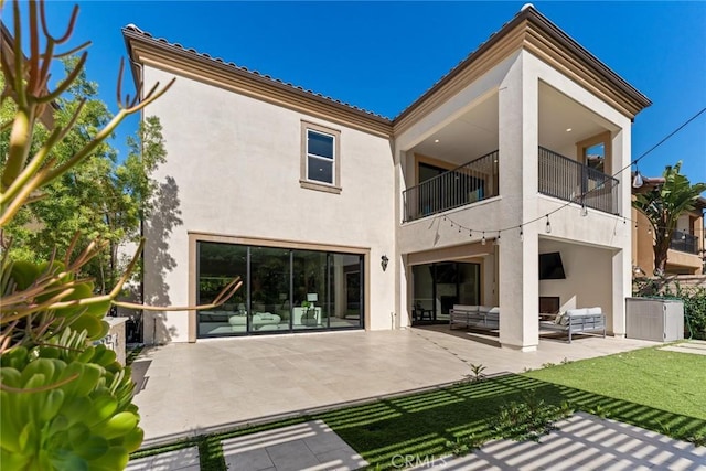 rear view of property featuring a lawn, a patio, a balcony, an outdoor hangout area, and stucco siding