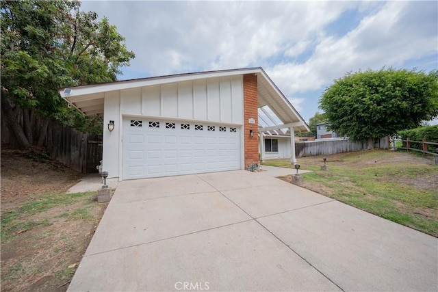 exterior space featuring an attached garage, fence, driveway, board and batten siding, and a front yard