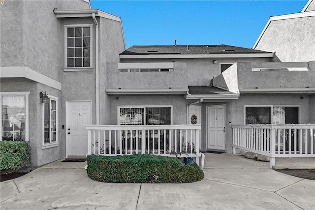 exterior space with covered porch, roof with shingles, and stucco siding